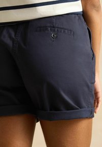 Marineblaue Baumwollshorts mit umgeschlagenem Saum, einer Gesäßtasche mit Knopf und einer glatten Textur. Der Stoff wirkt leicht.