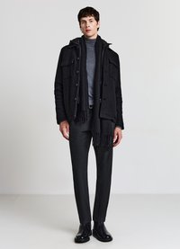 Outfit casual composto da un cappotto nero in lana con quattro tasche, un dolcevita grigio, una sciarpa nera, pantaloni neri testurizzati e stivali neri.