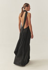 Vestido de satén negro con espalda baja, diseño de cuello halter y falda fluida. Cuenta con cremallera trasera y textura suave.