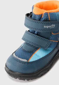 Blå og oransje vinterstøvel til barn med teksturert såle, to borrelåsremmer og "superfit"-merking på den øverste remmen.