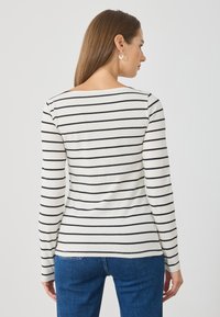 Langsleeve top van zachte katoen, met een crèmekleurige basis en horizontale zwarte strepen. Ronde halslijn en een aansluitend ontwerp, gecombineerd met blauwe jeans.