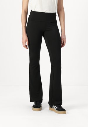 Black flared pants made of stretchy material with a high waistband. Worn with black sneakers featuring white stripes and a gum sole.