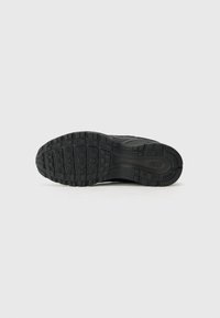 Čierna podrážka tenisky Nike s textúrovaným gumovým vzorom, obsahujúca drážky pre trakciu a hladkú oblasť päty pre stabilitu.