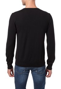 Maglione lavorato a maglia nero con scollatura rotonda e maniche lunghe, caratterizzato da un orlo a coste, indossato sopra a jeans blu.