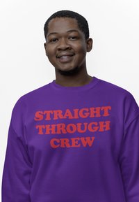 Fialová mikina s nápisem "STRAIGHT THROUGH CREW" v tučných červených písmenech. Měkká tkanina, kulatý výstřih a dlouhé rukávy.