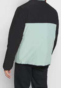 Veste matelassée avec une partie supérieure noire et une partie inférieure vert menthe, présentant une texture lisse et un ourlet élastiqué.