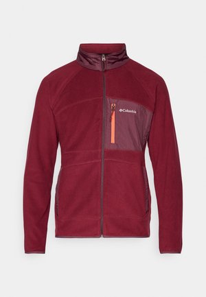 Maroon fleecejakke med en glidelåslomme på brystet som har en oransje glidelås. Høy krage med paneler i en lysere nyanse. Myk tekstur.