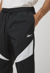 Schwarze Sporthose mit elastischem Bund, ausgestattet mit einem weißen diagonalen Akzent und Logo. Hergestellt aus leichtem, strukturiertem Material.