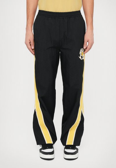 Μαύρο σορτς σπορ με ελαστική μέση, διαθέτοντας κίτρινες ρίγες και γραφιστικό σχέδιο στο μηρό. Φτιαγμένο από ελαφρύ ύφασμα.