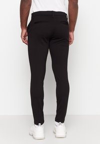 Zwarte slim-fit broek van een soepele stof, met een middelhoge tailleband en twee achterzakken. Gecombineerd met witte sneakers.