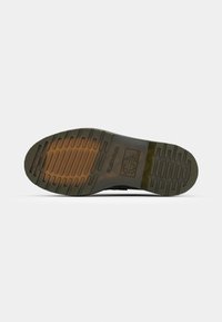 Semelle d'une botte translucide avec des motifs horizontaux de la bande de roulement et un logo présentant une croix et une icône d'arbre au centre.