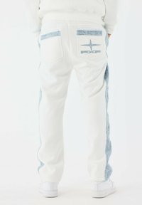Witte jogpants met lichtblauwe denim zijpanelen, twee achterzakken met blauwe accenten en geribbelde boorden bij de enkels.