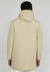 Chaqueta parka beige con capucha, de textura suave y forma alargada, con detalles de botones a presión en los puños. Vista trasera, sin patrones visibles.