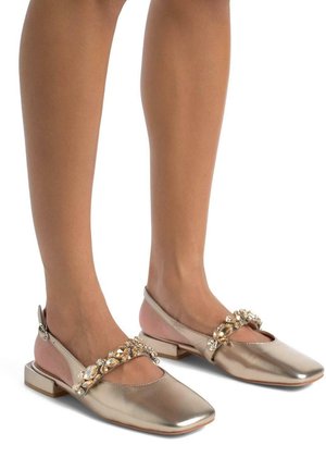 Metallic gold ballet flats with a square toe, embellished strap with clear gems, and a low block heel. Soft pink accent on the heel.