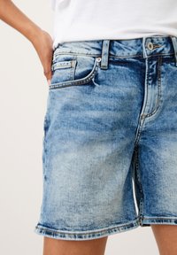 Světle modré džíny šortky se sepraným designem, vybavené pěti kapsami, kovovým tlačítkovým zapínáním a viditelným švem podél okrajů.