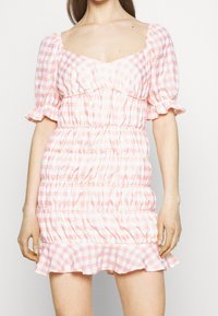 Abito a scacchi rosa e bianco con maniche a sbuffo, scollatura quadrata, corpino arricciato e orlo a volant, realizzato in tessuto leggero.
