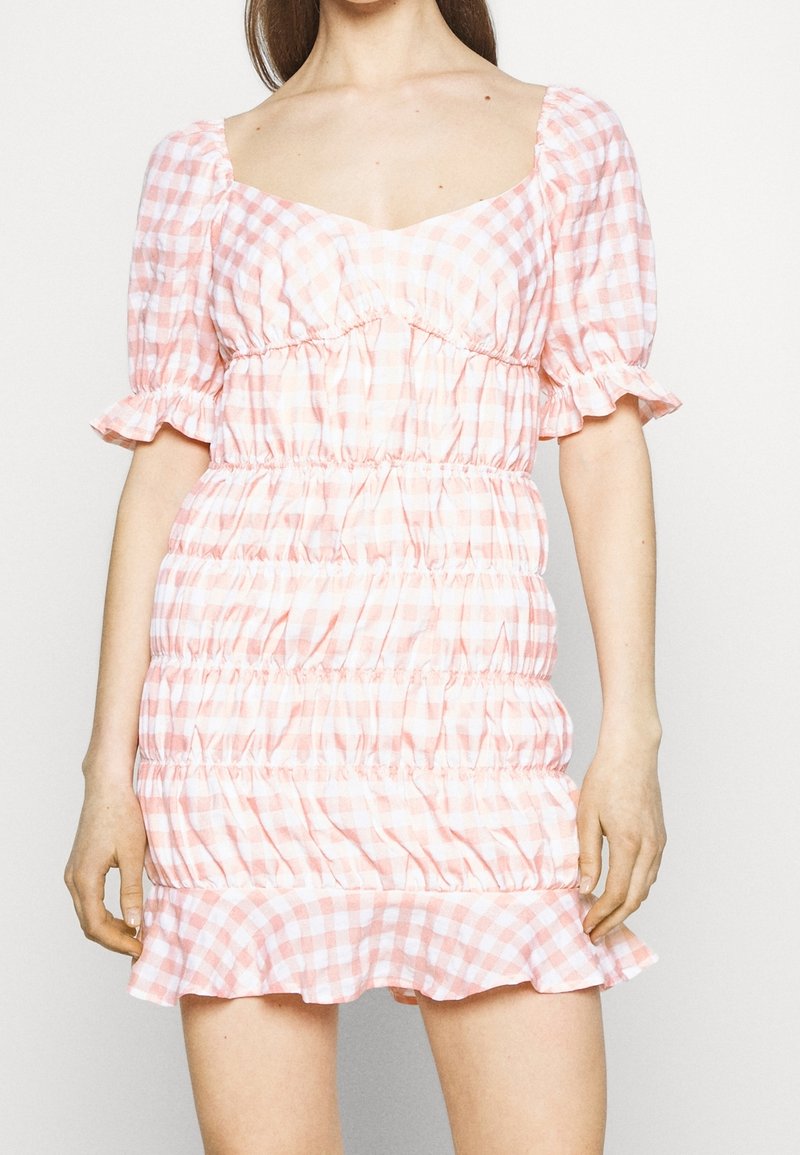 Abito a scacchi rosa e bianco con maniche a sbuffo, scollatura quadrata, corpino arricciato e orlo a volant, realizzato in tessuto leggero.