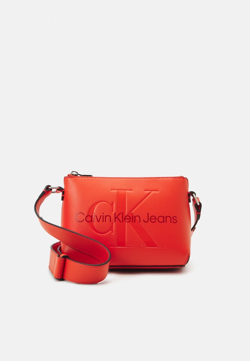Borsa a tracolla rossa sintetica con logo "CK" in rilievo e scritta "Calvin Klein Jeans". Presenta una tracolla staccabile e una superficie liscia.