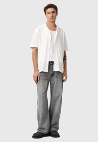 Hvid kortærmet skjorte med knapper, lagd over en hvid tanktop, parret med grå brede jeans og sorte sko. Simpelt design og afslappet pasform.