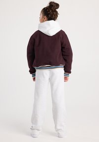 Maroon cropped jacket with a white hood, featuring ribbed cuffs and hem. Paired with light gray sweatpants, showing a relaxed fit and texture.