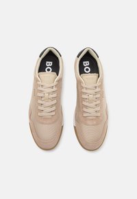 Beige joggesko med en blanding av mesh og semsket skinn, med snøring, svart hælakseent og brunt gummisåle.