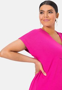 Fuchsiové šaty s výstřihem do V, krátkými rukávy a pohodlným střihem, s jemnými dekorativními akcenty a měkkou, hladkou texturou látky.