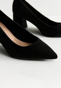 Scarpe con tacco alto in suede nero con punta affusolata e tacco largo. Presentano una superficie liscia e un design minimalista.