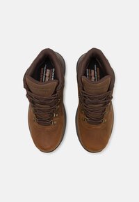 Zapatos de senderismo impermeables marrones con cuero texturizado, ojales de metal y cordones resistentes. Presentan una plantilla acolchada y una suela robusta.