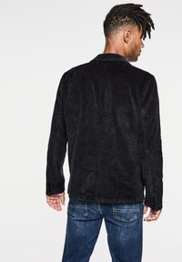 Svart manchestertäckjacka med skräddarsydd design, slagkrage och knäppte ärmar, i kombination med blå denimjeans. Texturerat tyg och slim fit.