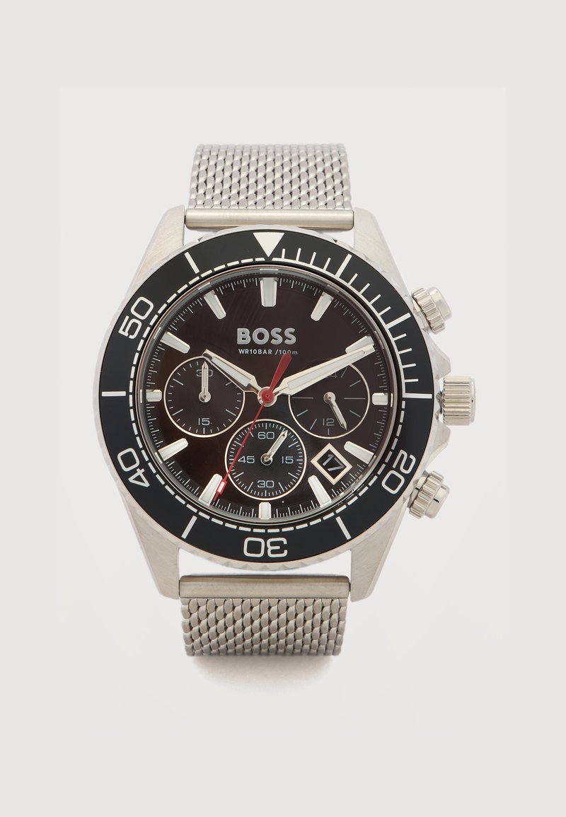 Reloj de pulsera BOSS plateado con bisel negro, esfera negra, tres subesferas, ventana de fecha y correa de malla metálica, mostrando la hora 10:10:37.
