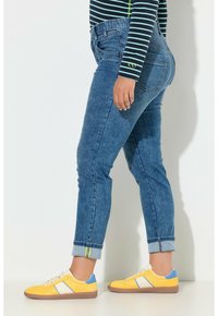 Siniset farkut, joissa on istuva malli, käännetyt lahkeet ja kaksi takataskua. Yhdistetty keltaisiin lenkkareihin, joissa on sinisiä ja valkoisia yksityiskohtia.