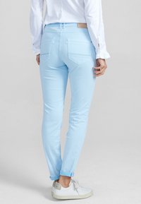 Pantalon en denim bleu clair à coupe fuselée, avec poches plaquées arrière et ourlets retroussés, associé à des baskets blanches.