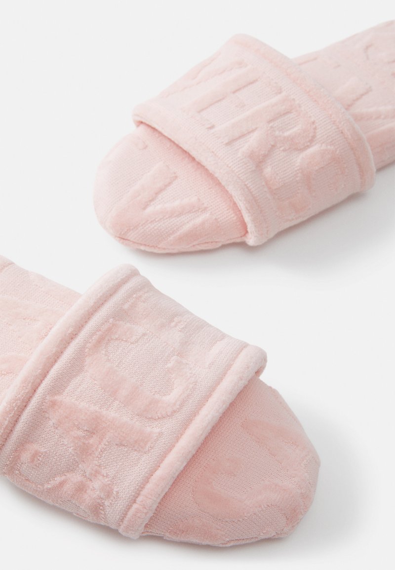 Infradito in tessuto rosa con texture soffice, caratterizzati da lettere in rilievo sulle fasce e zona della punta arrotondata, progettati per comfort e facilità d'uso.