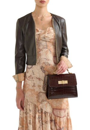 Giacca corta in pelle marrone, abito beige con stampa a mappa, che tiene una borsa in pelle stampata coccodrillo marrone scuro con dettagli dorati e manico superiore.