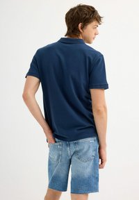Polo de color navy con mangas cortas y un cuello estándar, combinado con unos shorts de mezclilla azul claro que tienen bolsillos traseros y un dobladillo deshilachado.