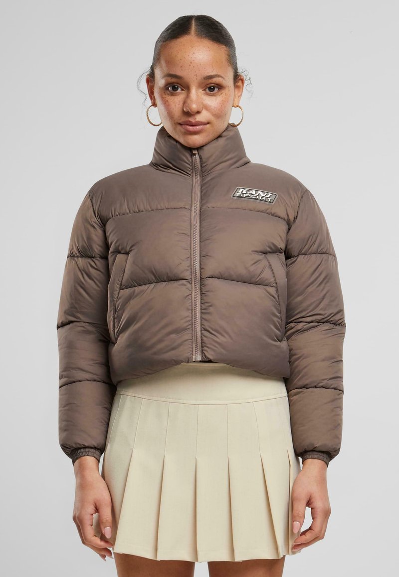 Smeđi skraćeni puffer kaput s visokim ovratnikom, zatvaranjem na zip, te logotipom, koji sadrži kviltane dijelove i elastične manžete.
