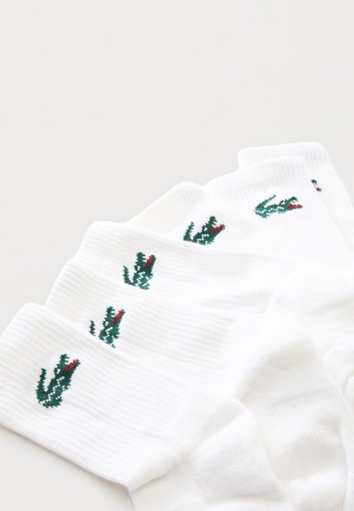Cinq paires de chaussettes blanches côtelées avec un petit logo crocodile brodé en vert et rouge près du haut du bord.