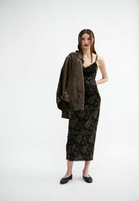 Schwarzes Blumen-Slipleid aus Samt mit Spitzenborte, kombiniert mit einer dunkelbraunen Lederjacke. Modell, das schwarze Ballerinas trägt und aufrecht steht.