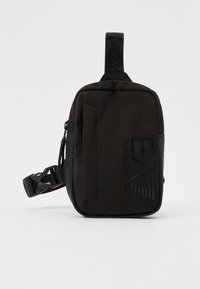 Black fabric shoulder bag with a rectangular shape, featuring a zip closure, adjustable strap, and embossed logo detail on the front.