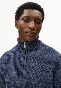 Marineblauer Strickpullover mit hohem Kragen und halbzipper Verschluss, mit strukturierter Musterung und kontrastierenden hellblauen Akzenten.