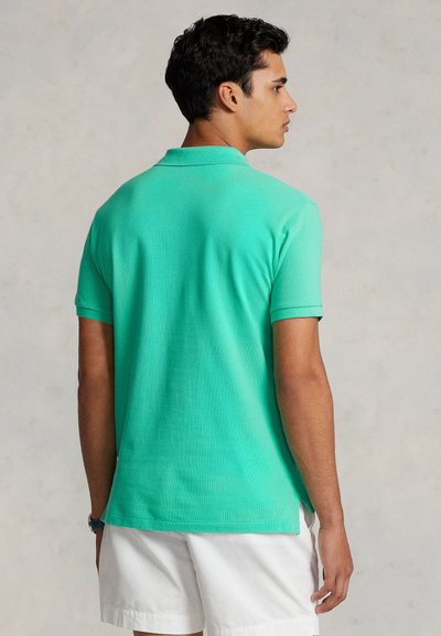 Πράσινο πόλο μπλουζάκι με κοντά μανίκια και γιακά, κατασκευασμένο από υφασμένο βαμβάκι. Πλαϊνές σχισμές στο κάτω μέρος για ευκολία κινήσεων. Απλός, καθαρός σχεδιασμός.