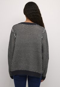 Džemperis ar tumši zilām un krēmkrāsas rūtiņām, ar ribotu apkakli un apakšmalu, kā arī brīvu piegriezumu. Mīksta adīta tekstūra.