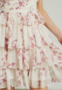 Sukienka w kwiatowy print z kremowym tłem, z warstwowymi falbanami, różowymi kwiatami, teksturowanym materiałem i zaciśniętym fasonem w talii.