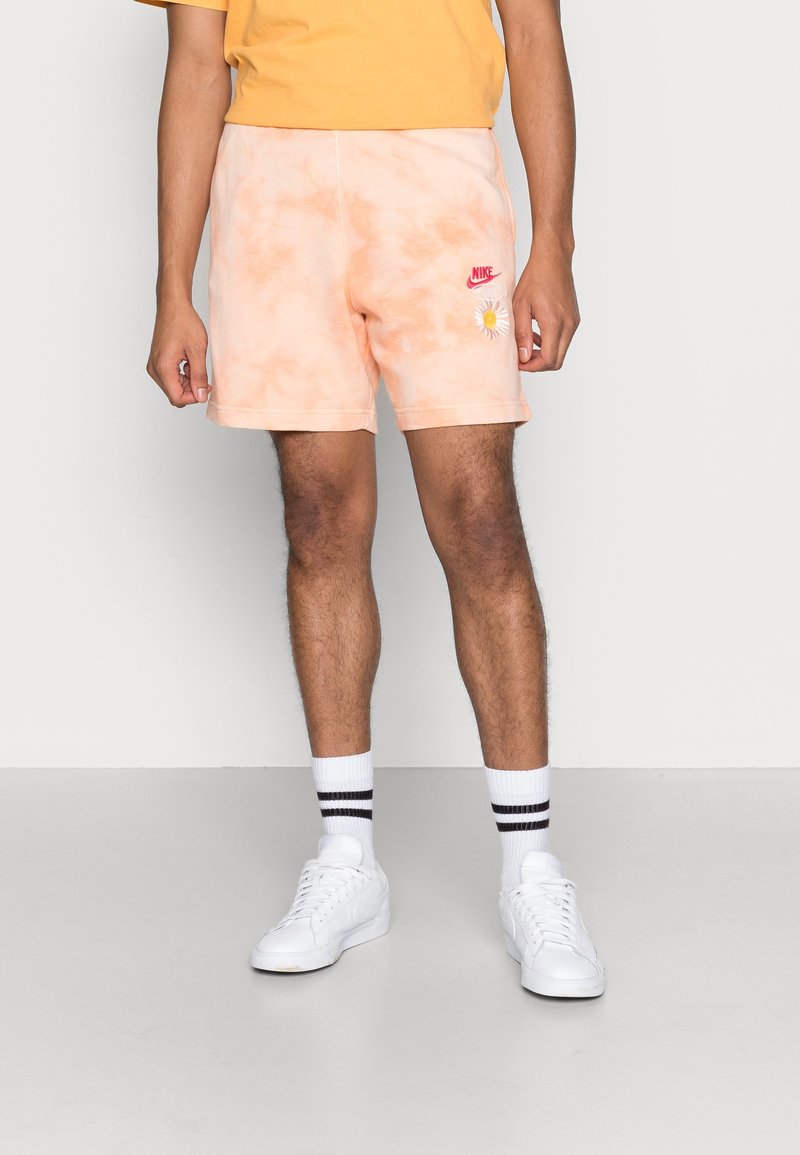 Shorts Nike en tie-dye de color melocotón claro, con un sol bordado y el logo. Combinados con zapatillas blancas y calcetines con rayas negras.