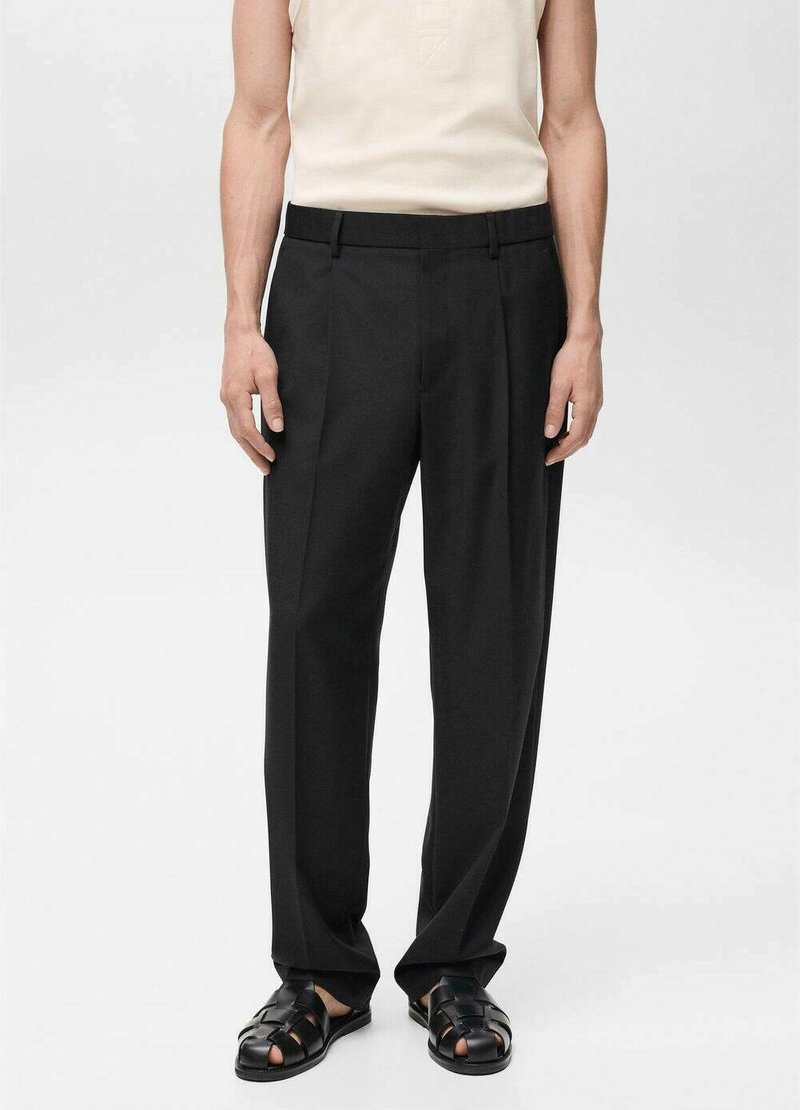 Pantalones negros de corte recto, con una tela suave, pliegues frontales y una cintura con trabillas para cinturón. Combinados con una blusa beige clara y sandalias negras.