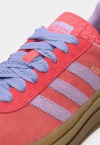 Κόκκινο και λεβαντίνι δερμάτινο αθλητικό παπούτσι με τρεις ρίγες και μαξιλαρωμένη γλώσσα, με ανοιχτό μοβ κορδόνια και υφασμένη ροζ φτέρνα.