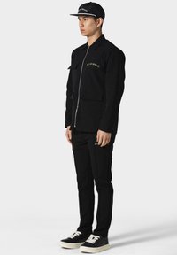 Mustaga jacket, millel on lukuga esiosa, kaks rinna taskut ja kuldne logo. Mustad püksid külglogo ja mustade spordijalatsitega, millele lisab must müts.