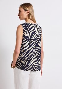 Sleeveless top featuring a navy and cream zebra print, made from lightweight fabric with a soft texture. Rounded hem and button closure at the back.