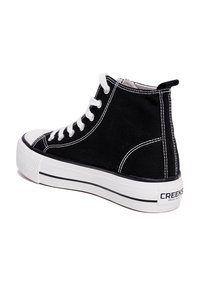 Zwarte hoge sneakers met witte veters, contrasterende stiksels en een dikke witte zool. Logo zichtbaar op de hiel. Textuurcanvas materiaal.