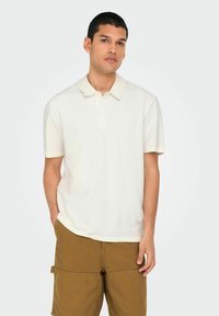 Cremefarvet polo T-shirt med korte ærmer, tekstureret stof og klassisk krave. Båret med khaki cargo shorts med lommer.
